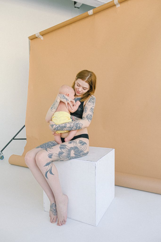 young tattooed mother in underwear embracing newborn baby in jpg 1